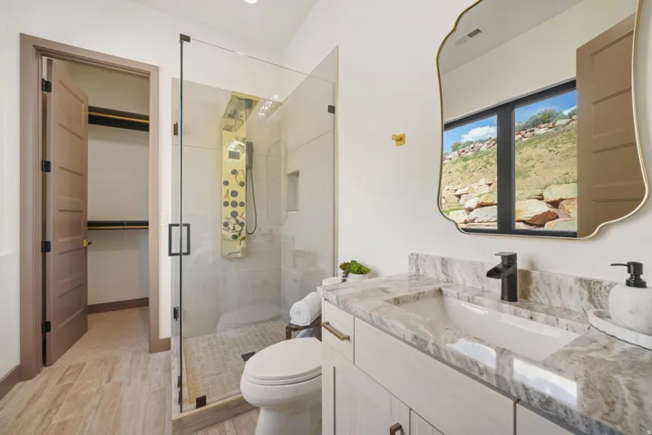 Bathroom featuring a frameless glass shower enclosure with a multi-jet shower panel, a white vanity with a rectangular undermount sink, a marble-look countertop, and a modern black faucet