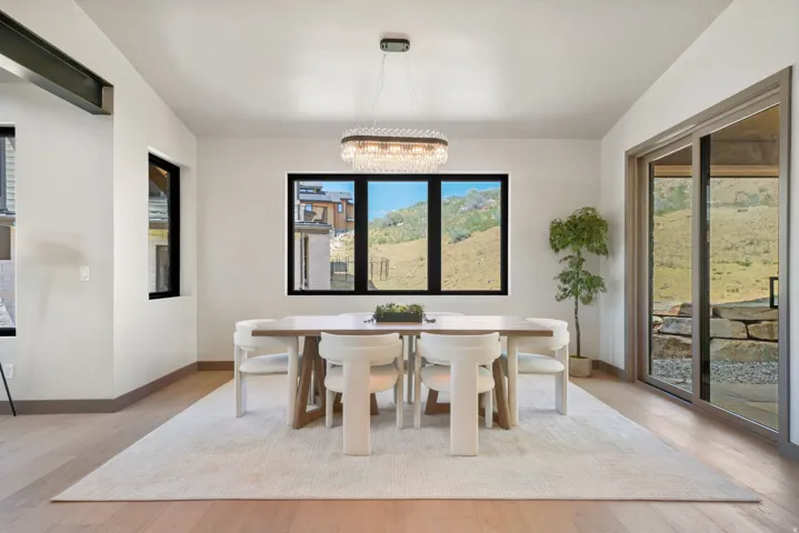 Dining area featuring light wood-finish flooring, a contemporary chandelier, multiple windows with black trim, and a sliding glass door