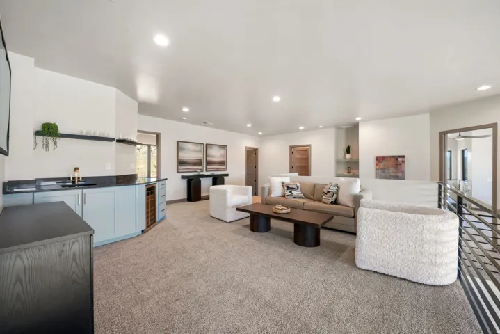 Spacious open-concept living area featuring a built-in wet bar with light blue cabinetry, a beverage refrigerator, and a gold-tone faucet