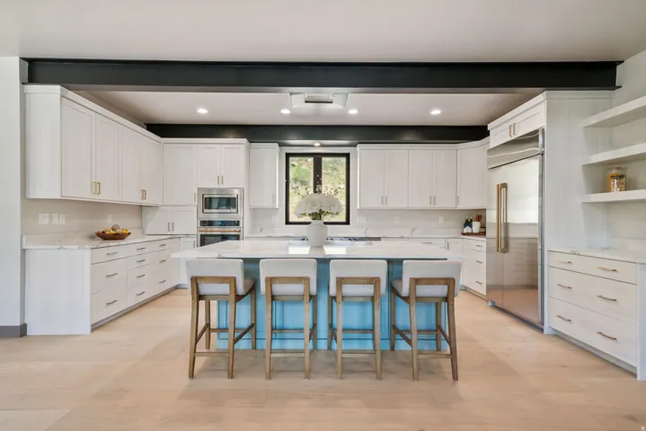 Contemporary kitchen featuring a light wood-finish floor, white cabinetry, integrated stainless steel appliances, and a central island with a light blue base and white countertop