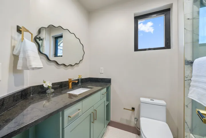Bathroom featuring a mint green vanity with a dark countertop, an undermount sink with a gold-tone faucet, a decorative mirror, and a window with a black frame