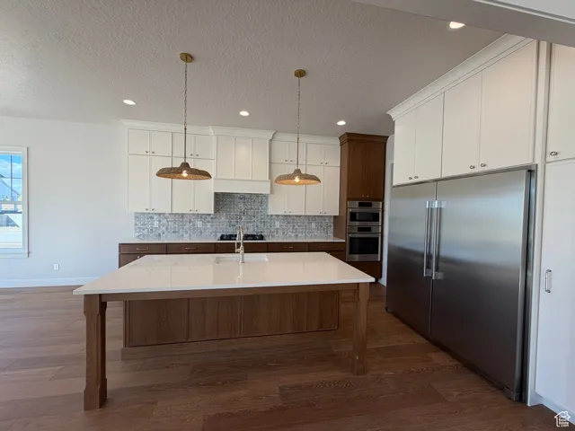 Kitchen featuring stainless steel appliances, white cabinets, hanging light fixtures, a kitchen island with sink, and a textured ceiling