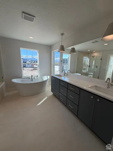 Full bath featuring a shower stall, double vanity, a textured ceiling, a freestanding tub, and light tile patterned floors