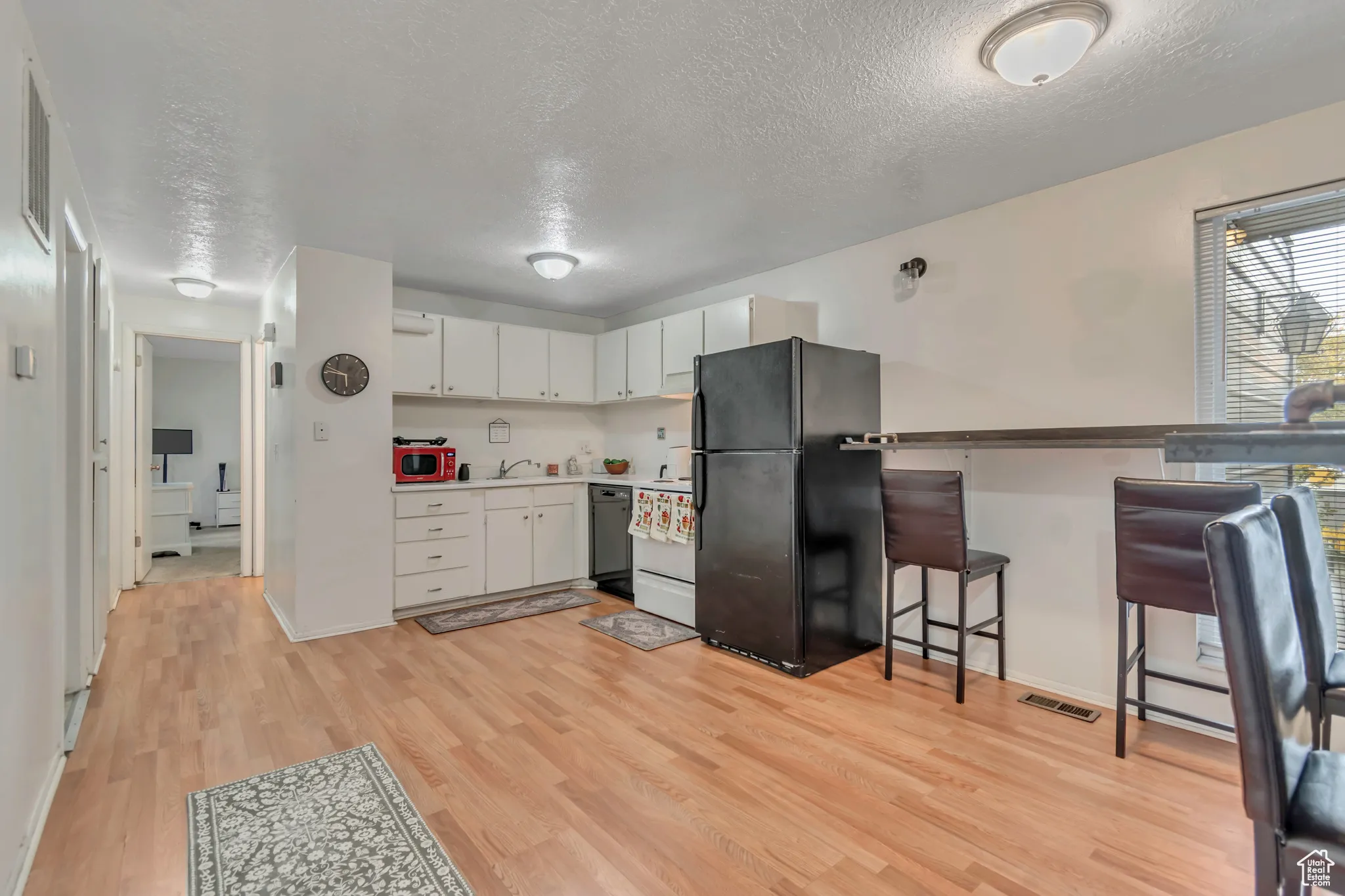 Kitchen featuring black appliances, a textured ceiling, light wood-type flooring, white cabinets, and light countertops