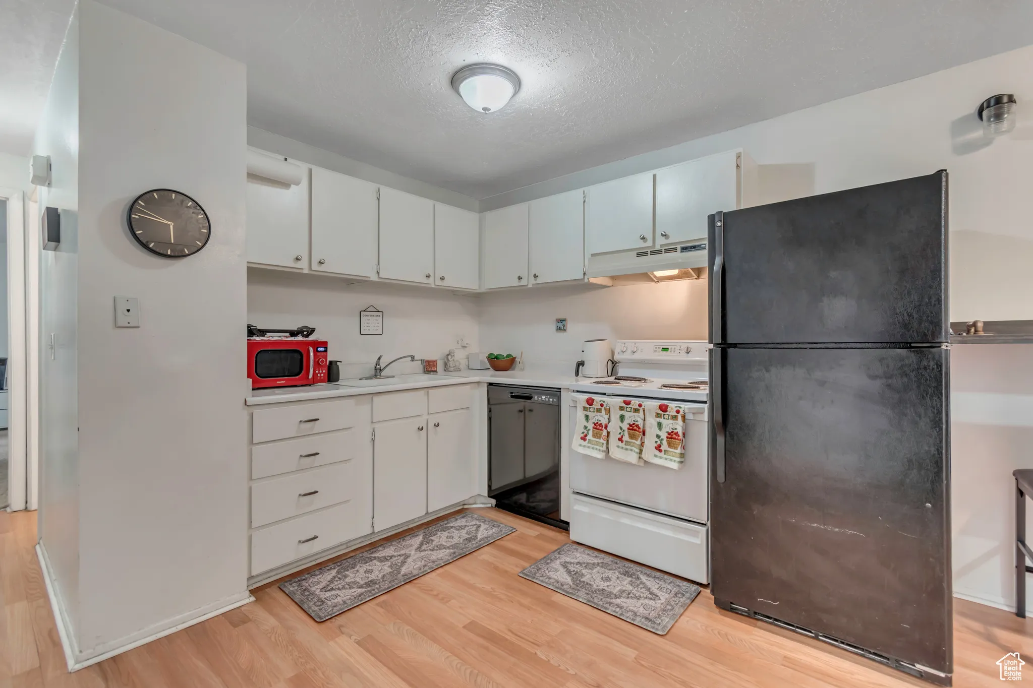 Kitchen with black appliances, a textured ceiling, light countertops, white cabinets, and light wood finished floors