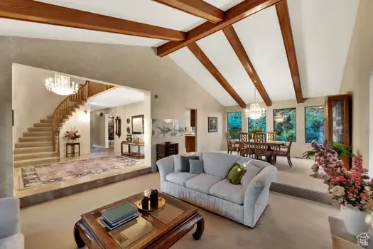Living room featuring a chandelier, carpet floors, stairs and dramatic vaulted beamed ceilings.