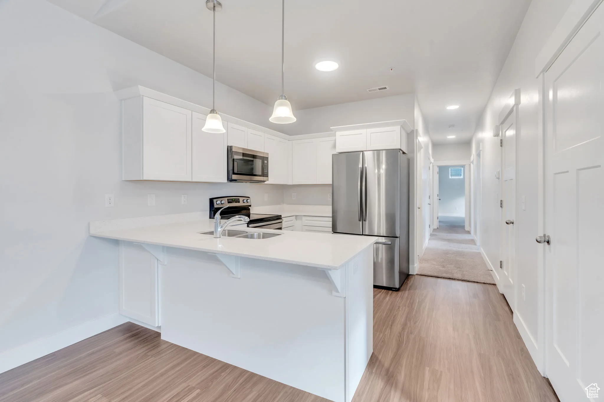 Kitchen featuring stainless steel appliances, white cabinetry, pendant lighting, a peninsula, and quartz counter tops.