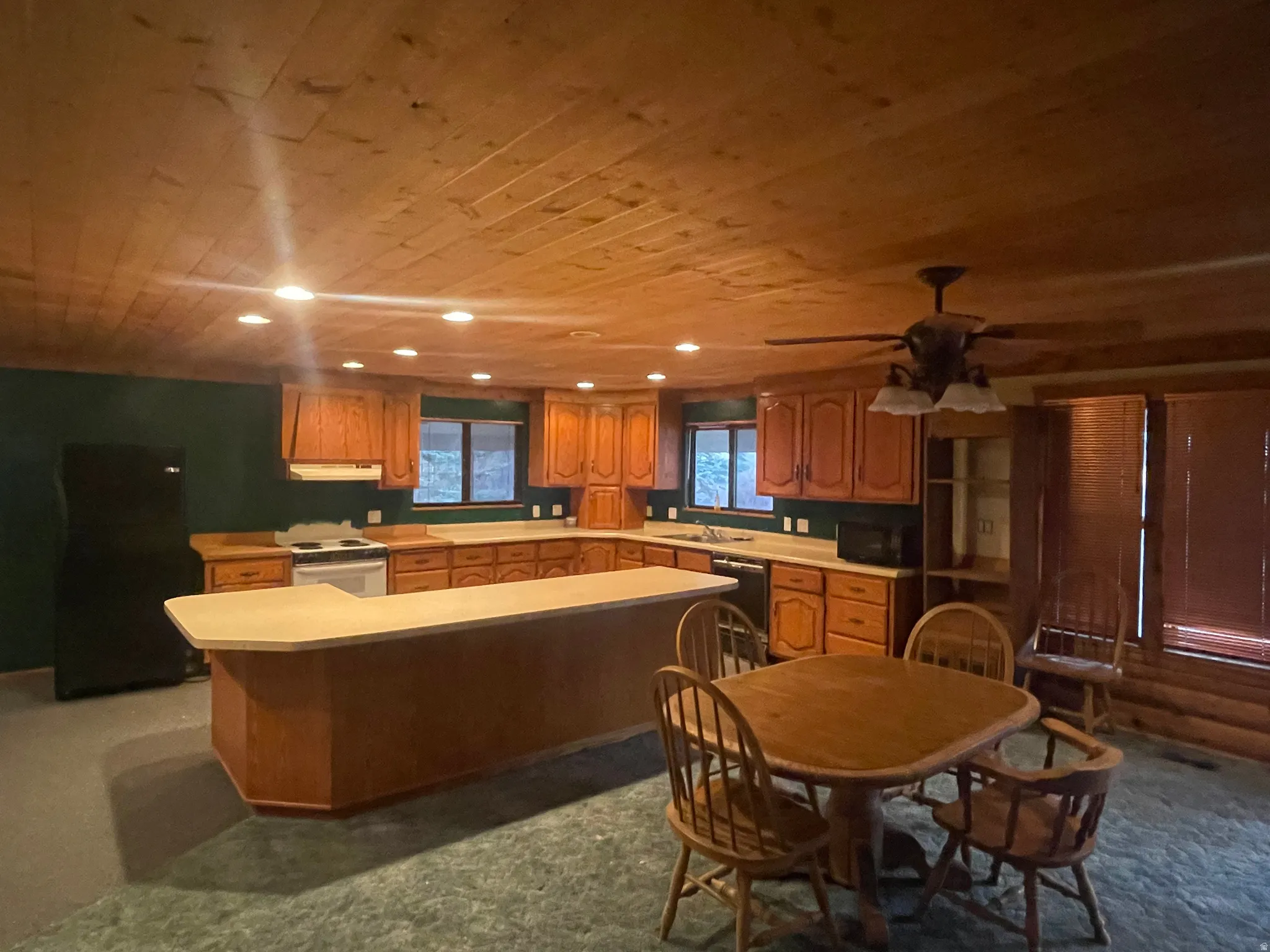 Kitchen with wooden ceiling, light countertops, black appliances, a center island, and brown cabinetry