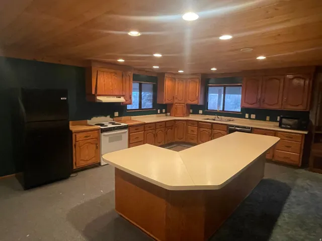 Kitchen with light countertops, freestanding refrigerator, white range with electric stovetop, brown cabinetry, and wooden ceiling