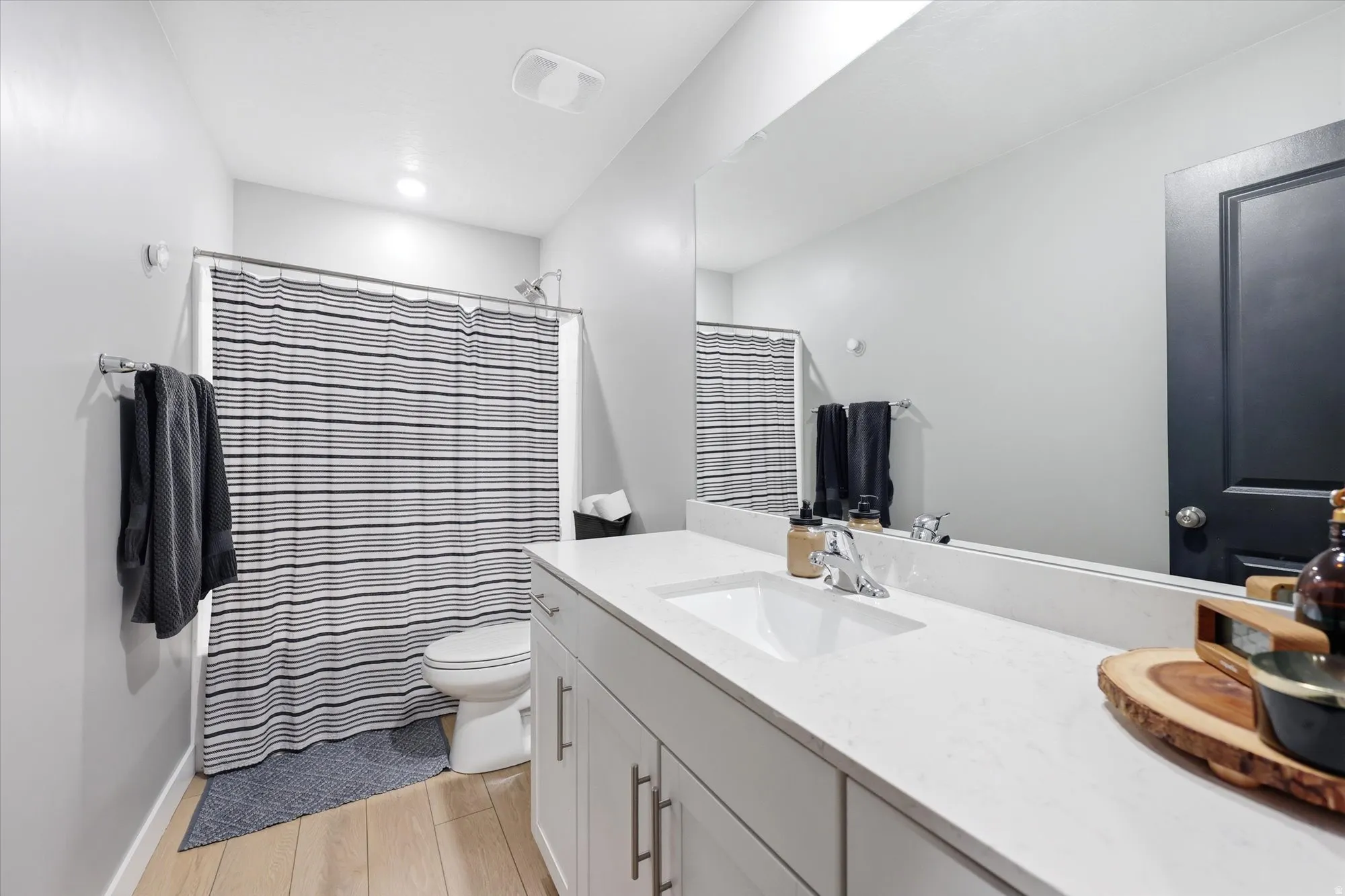 Contemporary bathroom featuring a spacious vanity with an integrated sink, a large wall-mounted mirror, and wood-finish flooring