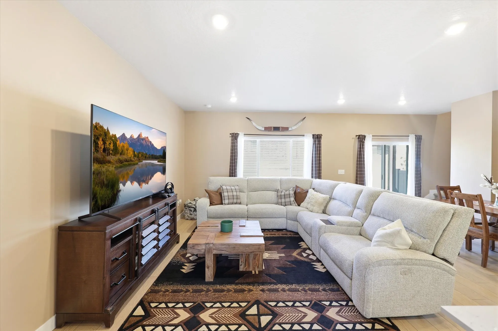Open-concept living area featuring light wood-finish flooring, recessed ceiling lighting, and a large window with blinds