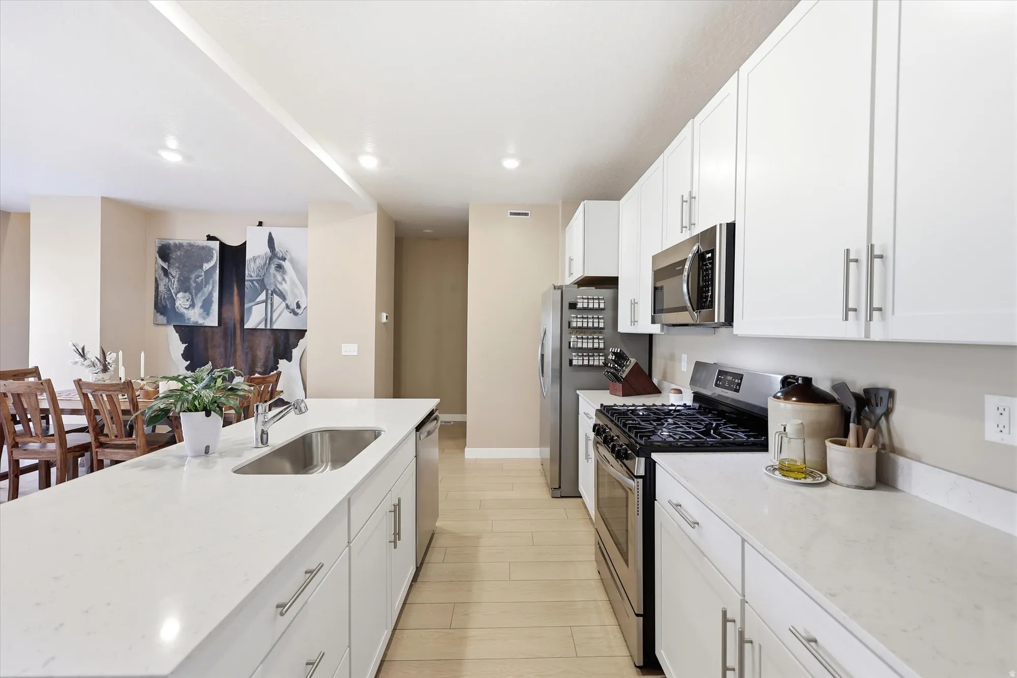 Modern kitchen featuring white cabinetry, light countertops, stainless steel appliances, and wood-finish flooring