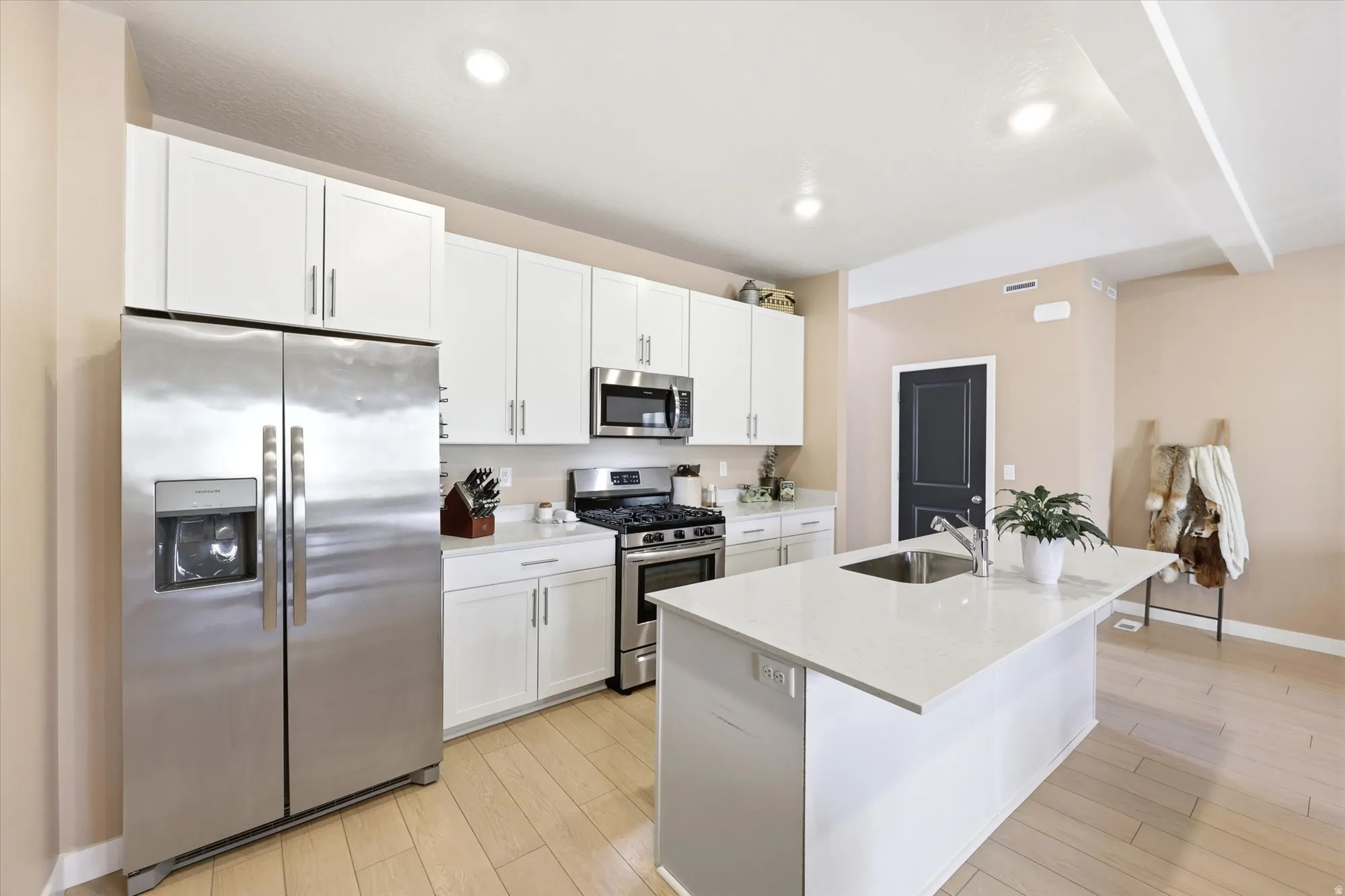 Modern kitchen featuring light wood-finish flooring, white cabinetry, stainless steel appliances, and a central island with a sink