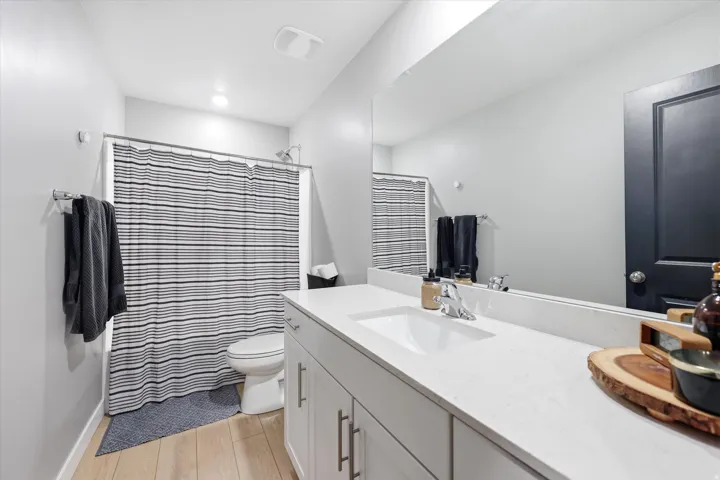 Contemporary bathroom featuring a spacious vanity with an integrated sink, a large wall-mounted mirror, and wood-finish flooring