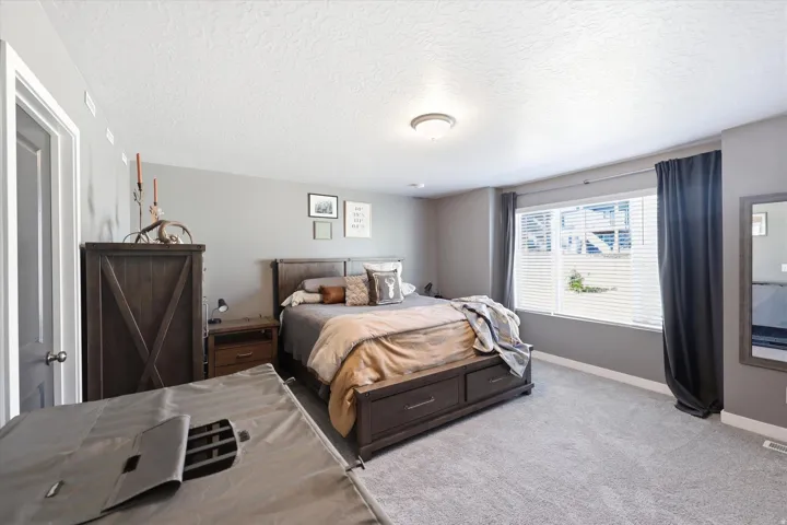 Spacious room featuring neutral gray walls, light gray carpeting, and a large window with white blinds and dark curtains