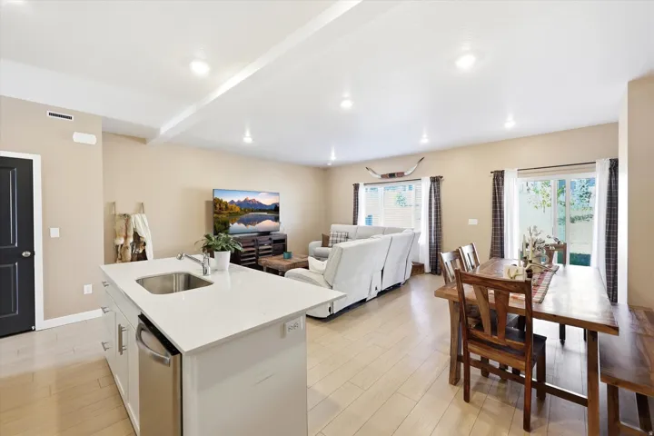 Open-concept living space featuring a central kitchen island with integrated sink, light wood-finish flooring, recessed lighting, and sliding glass doors providing access to the outdoors