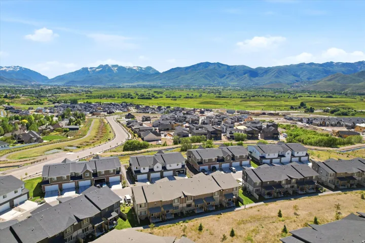 Expansive residential development featuring contemporary townhomes, varied architectural styles, paved roadways, and surrounding natural landscapes with distant mountains
