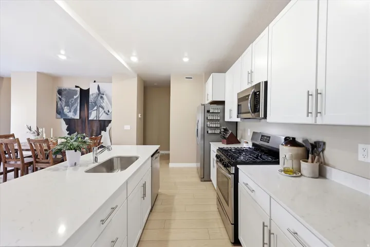 Modern kitchen featuring white cabinetry, light countertops, stainless steel appliances, and wood-finish flooring