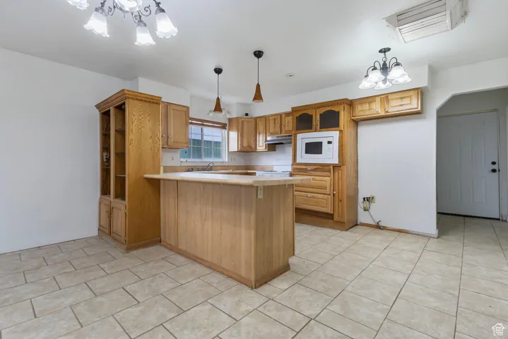 Kitchen with a chandelier, a peninsula, light countertops, decorative light fixtures, and white appliances