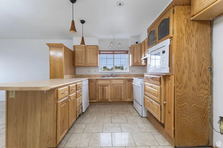 Kitchen with a peninsula, light countertops, light tile patterned flooring, white appliances, and brown cabinetry
