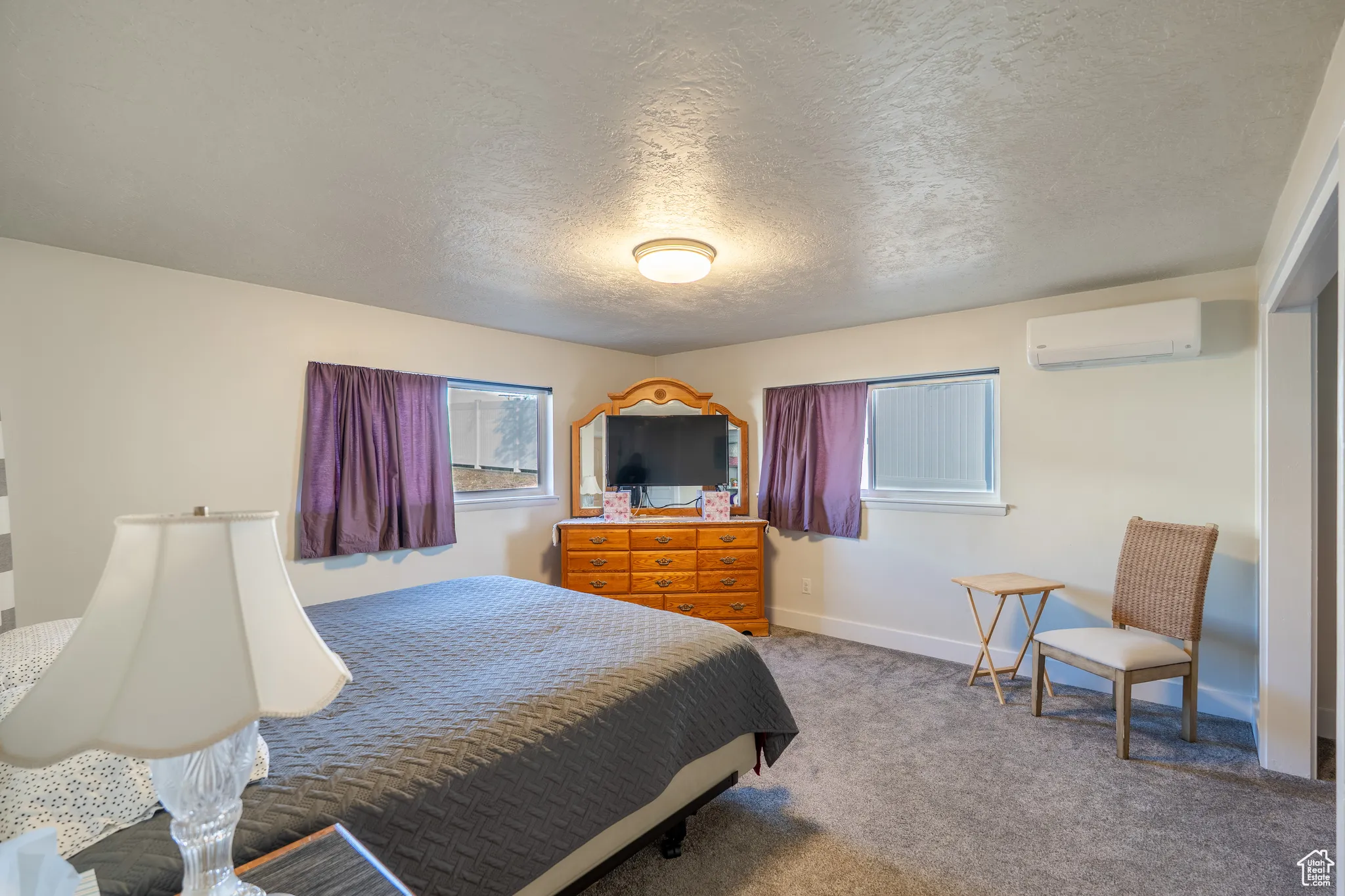 Bedroom with light carpet, a textured ceiling, and a wall mounted air conditioner