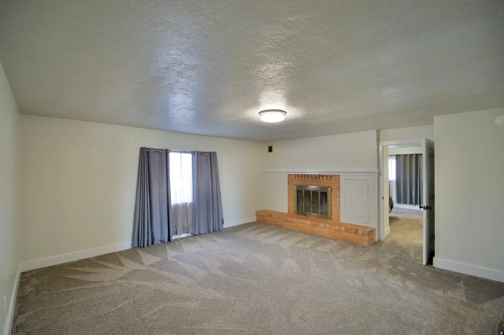 Spacious room featuring a brick-surround fireplace with a hearth, neutral carpet, and a ceiling-mounted light fixture