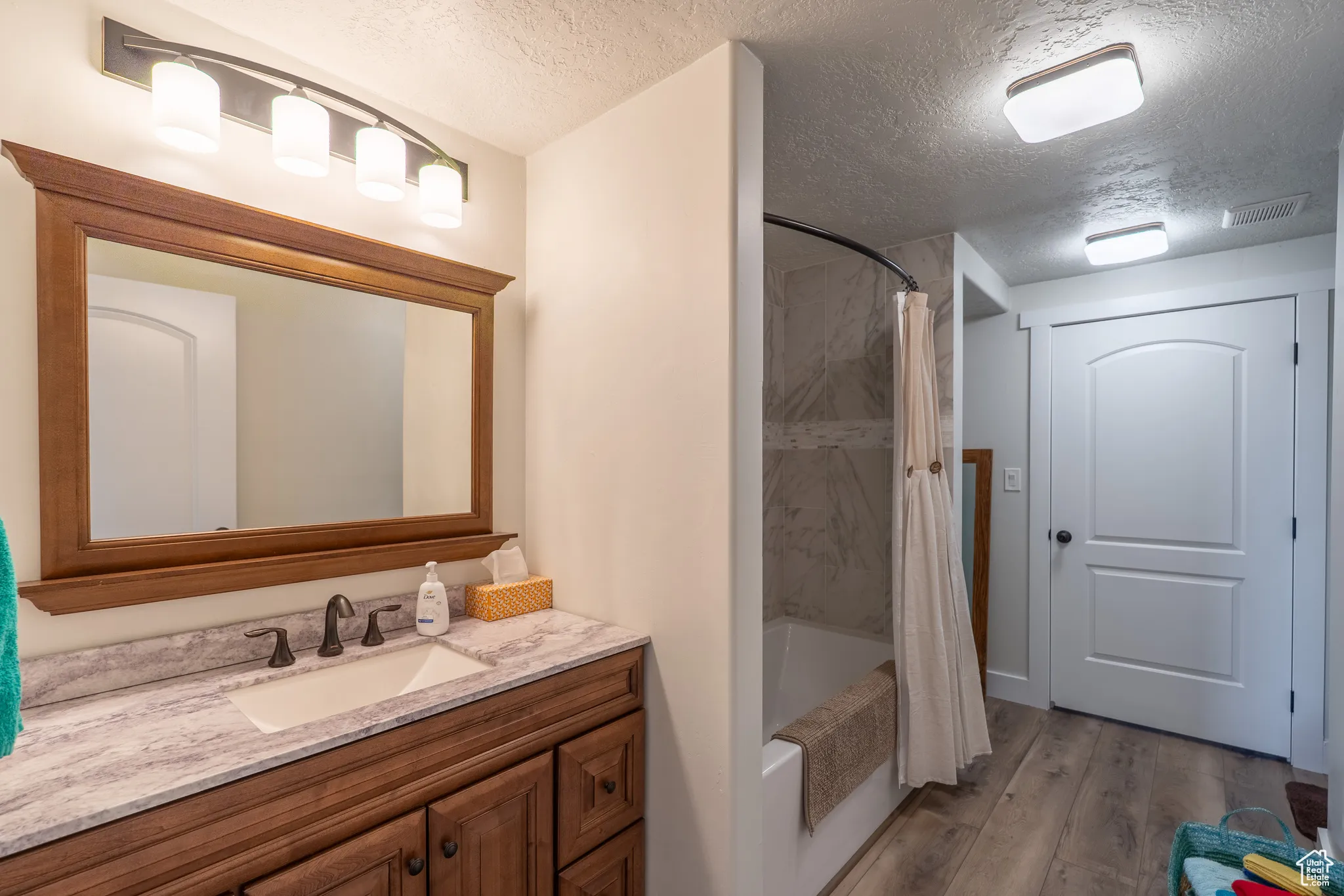 Full bathroom featuring shower / tub combo, a textured ceiling, vanity, and light wood finished floors