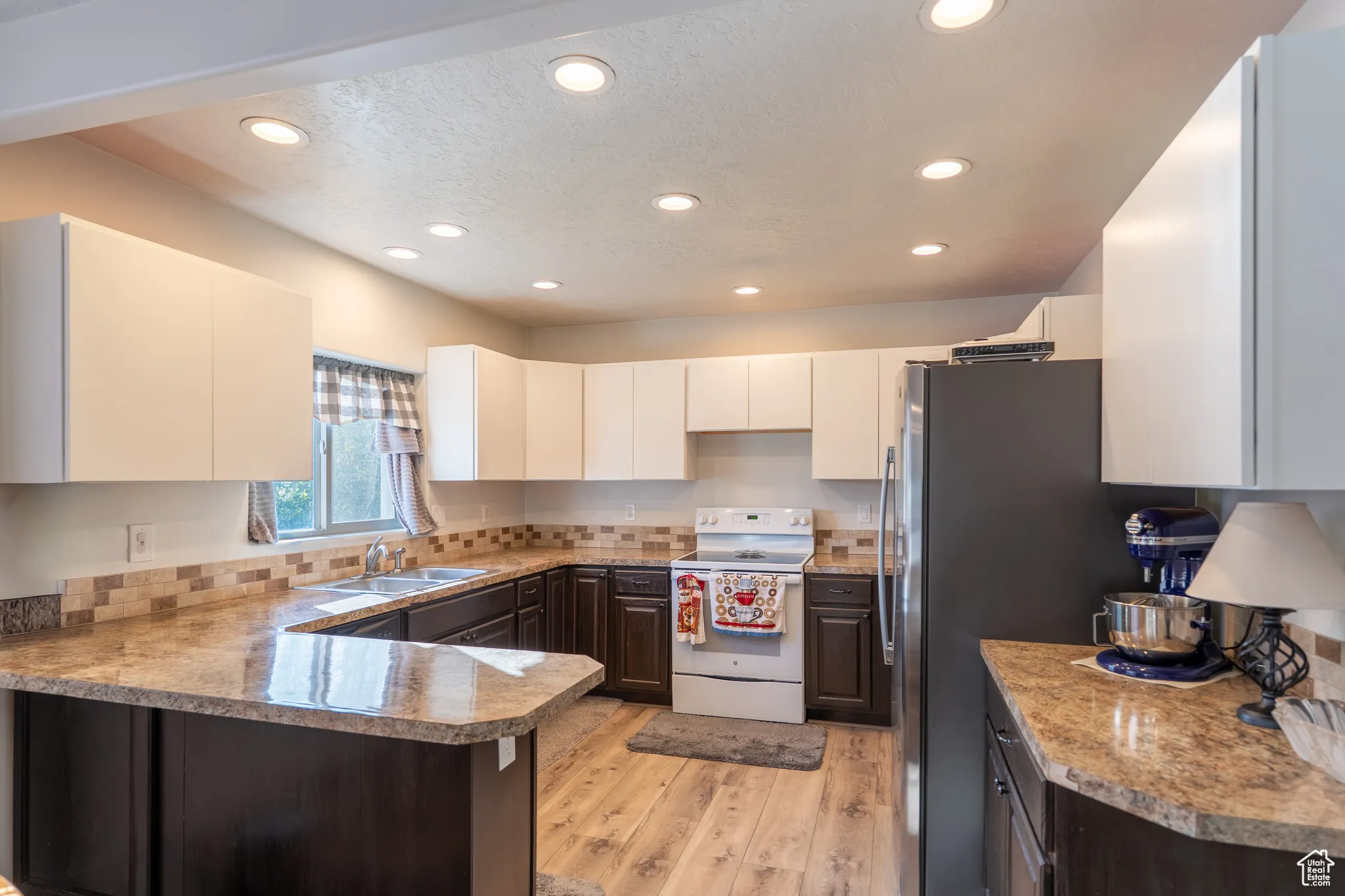 Kitchen featuring white range with electric stovetop, recessed lighting, light wood-style flooring, a peninsula, and freestanding refrigerator