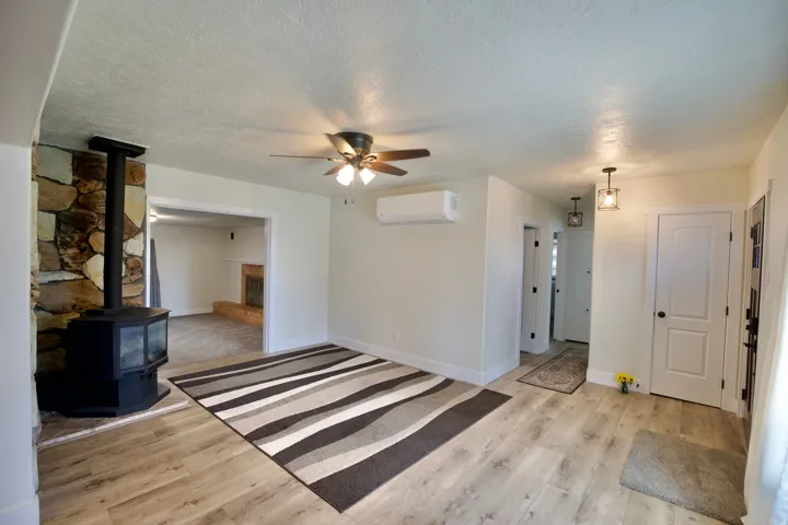 Stone-faced fireplace with wood-burning stove, wood-finish flooring, ceiling fan, and mini-split system