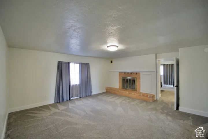 Spacious room featuring a brick-surround fireplace with a hearth, neutral carpet, and a ceiling-mounted light fixture