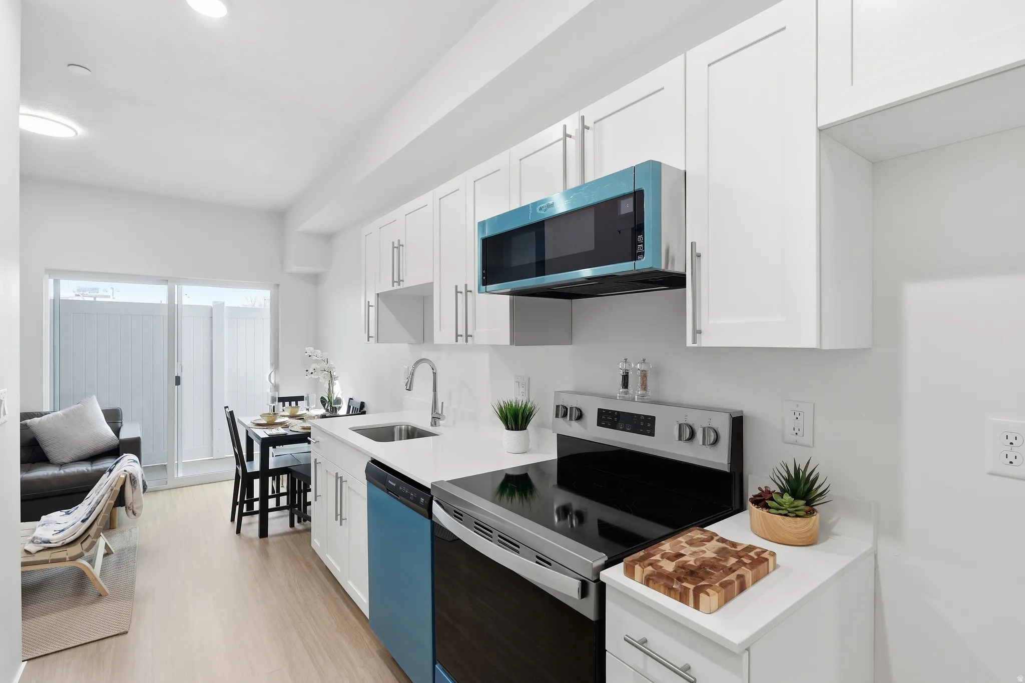 Kitchen with stainless steel electric stove, white cabinetry, dishwasher, light wood-type flooring, and light stone countertops