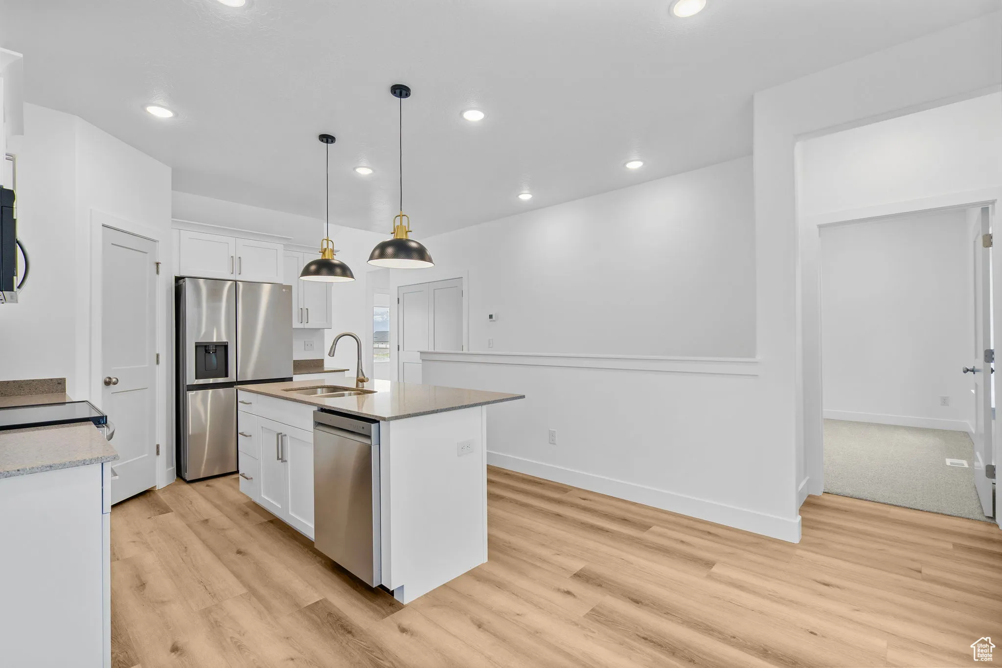 Kitchen featuring pendant lighting, recessed lighting, appliances with stainless steel finishes, white cabinetry, and an island with sink