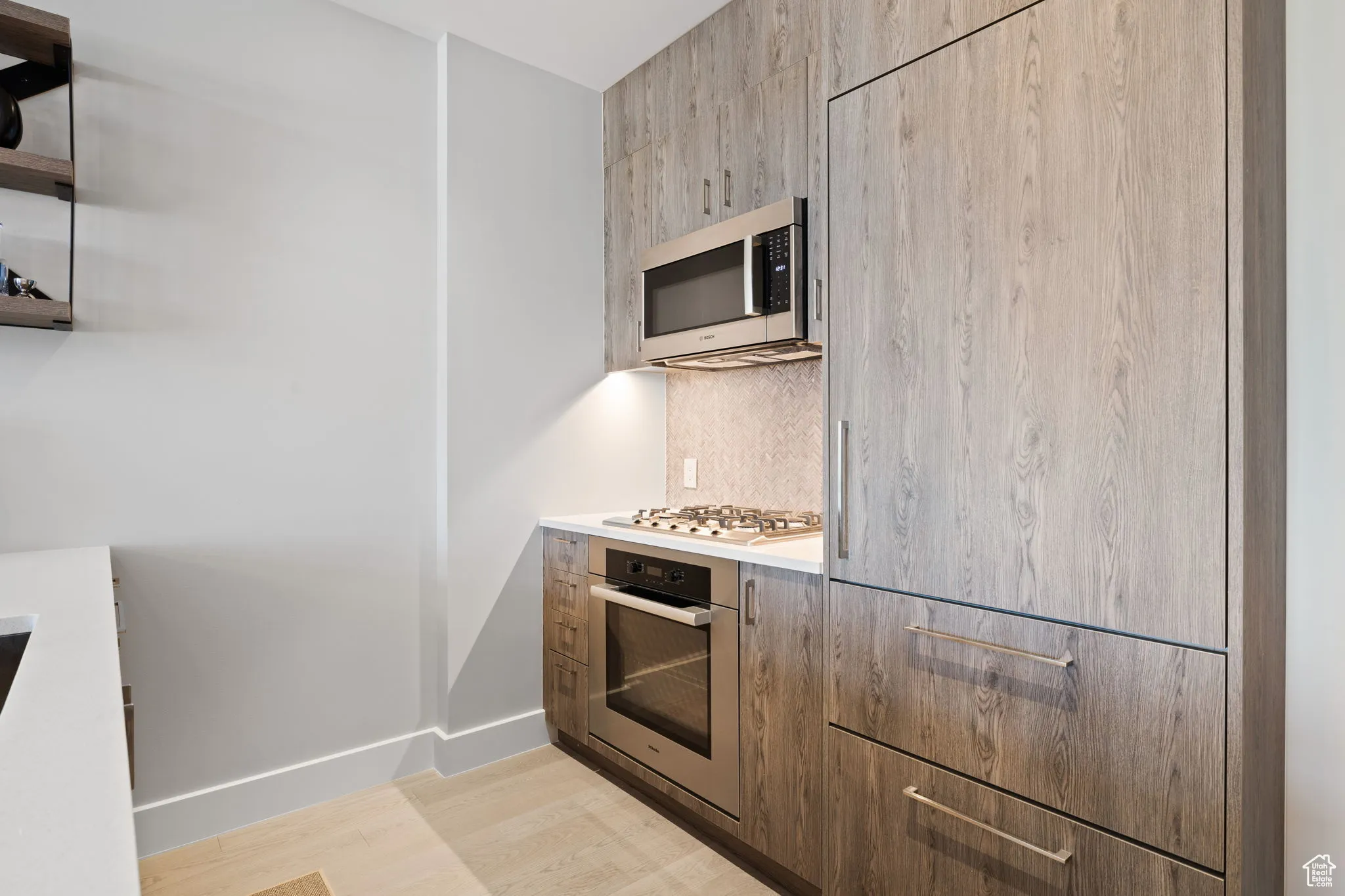 Kitchen featuring tasteful backsplash, modern cabinets, stainless steel appliances, light countertops, and light wood finished floors