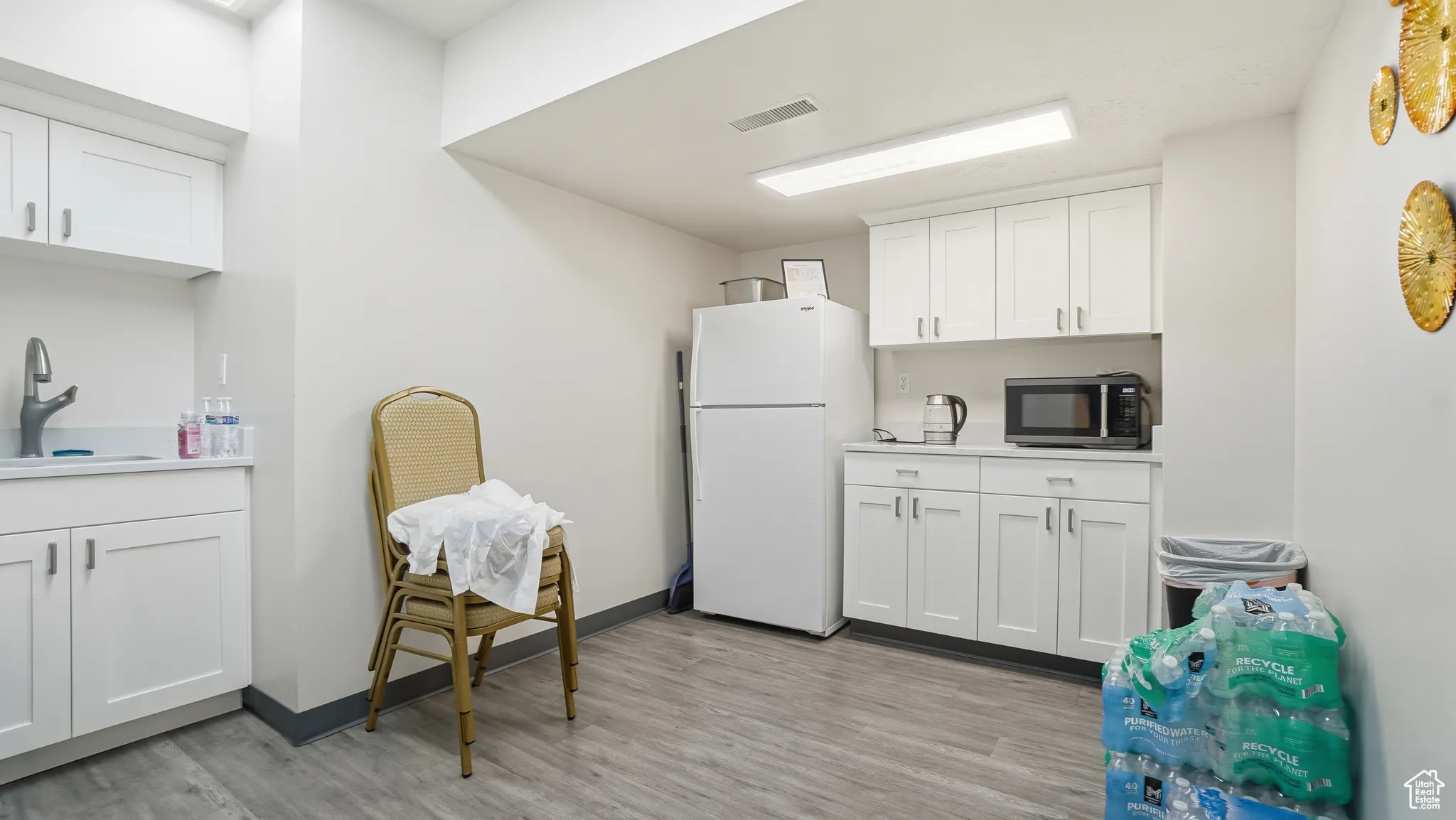 Kitchen with freestanding refrigerator, white cabinets, black microwave, light countertops, and light wood finished floors