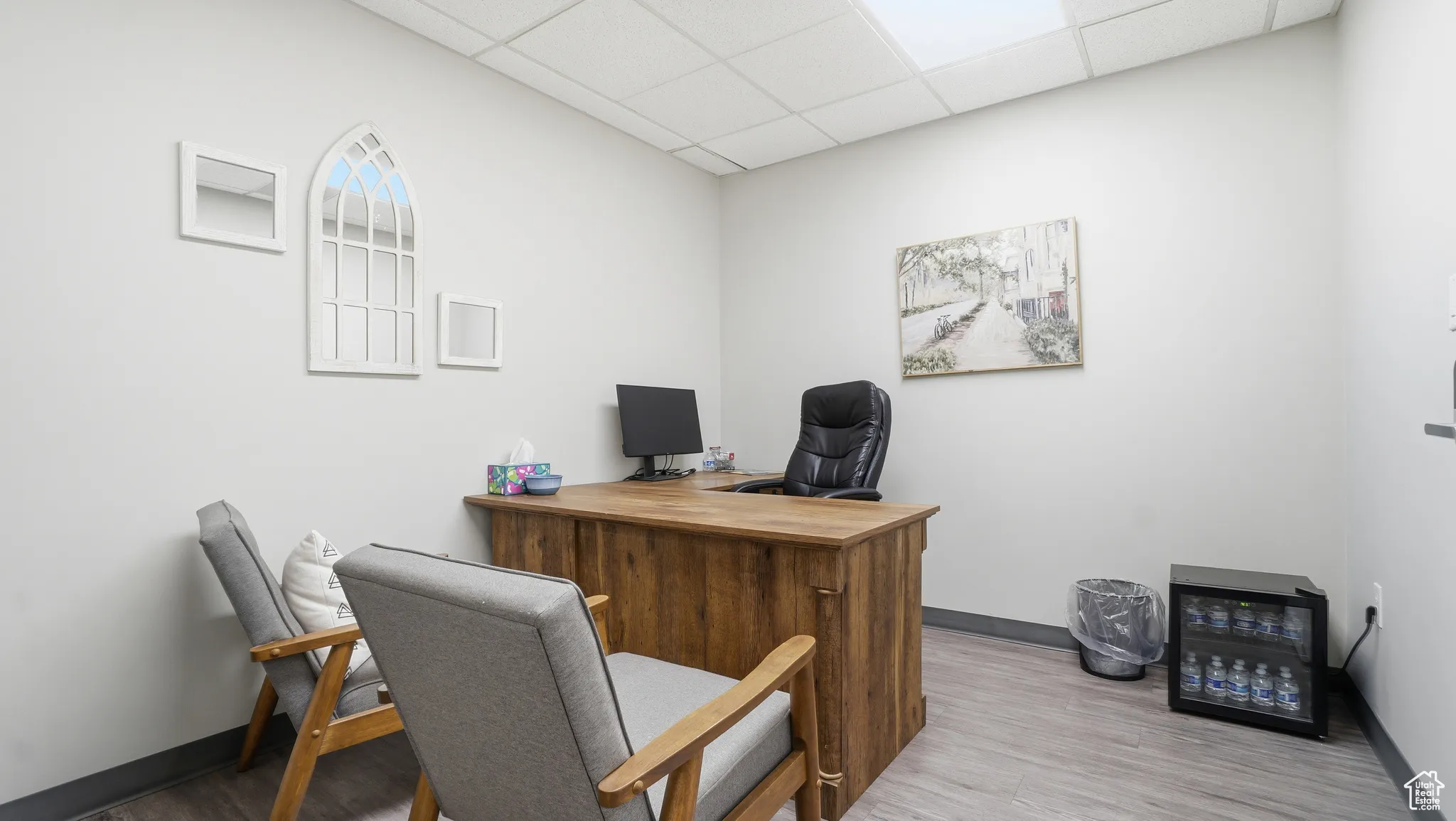Office space with a drop ceiling, wood finished floors, and beverage cooler