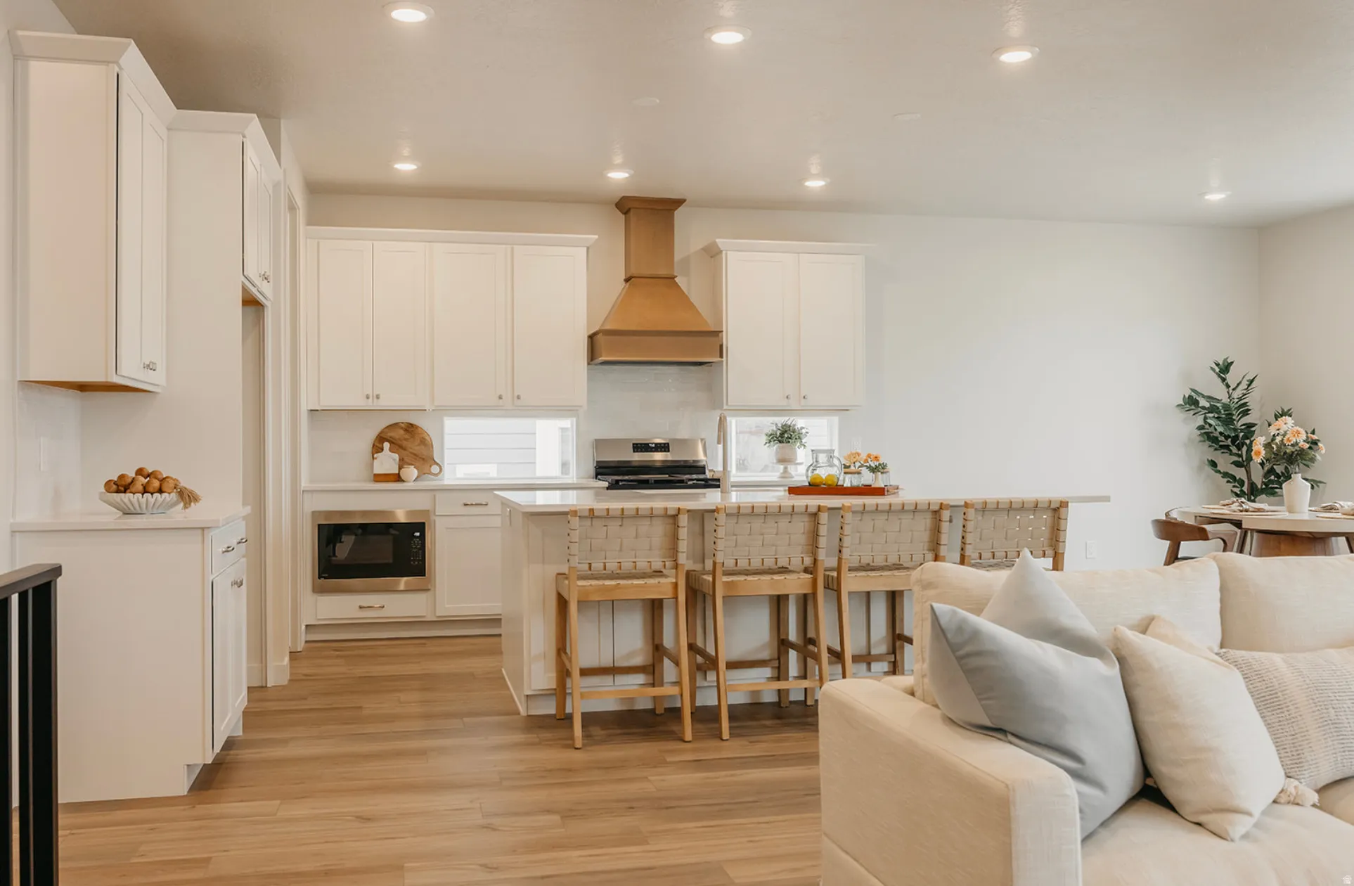 Open-concept kitchen featuring white cabinetry, a built-in microwave, a large island with seating, a wood-finish range hood, and wood-finish flooring