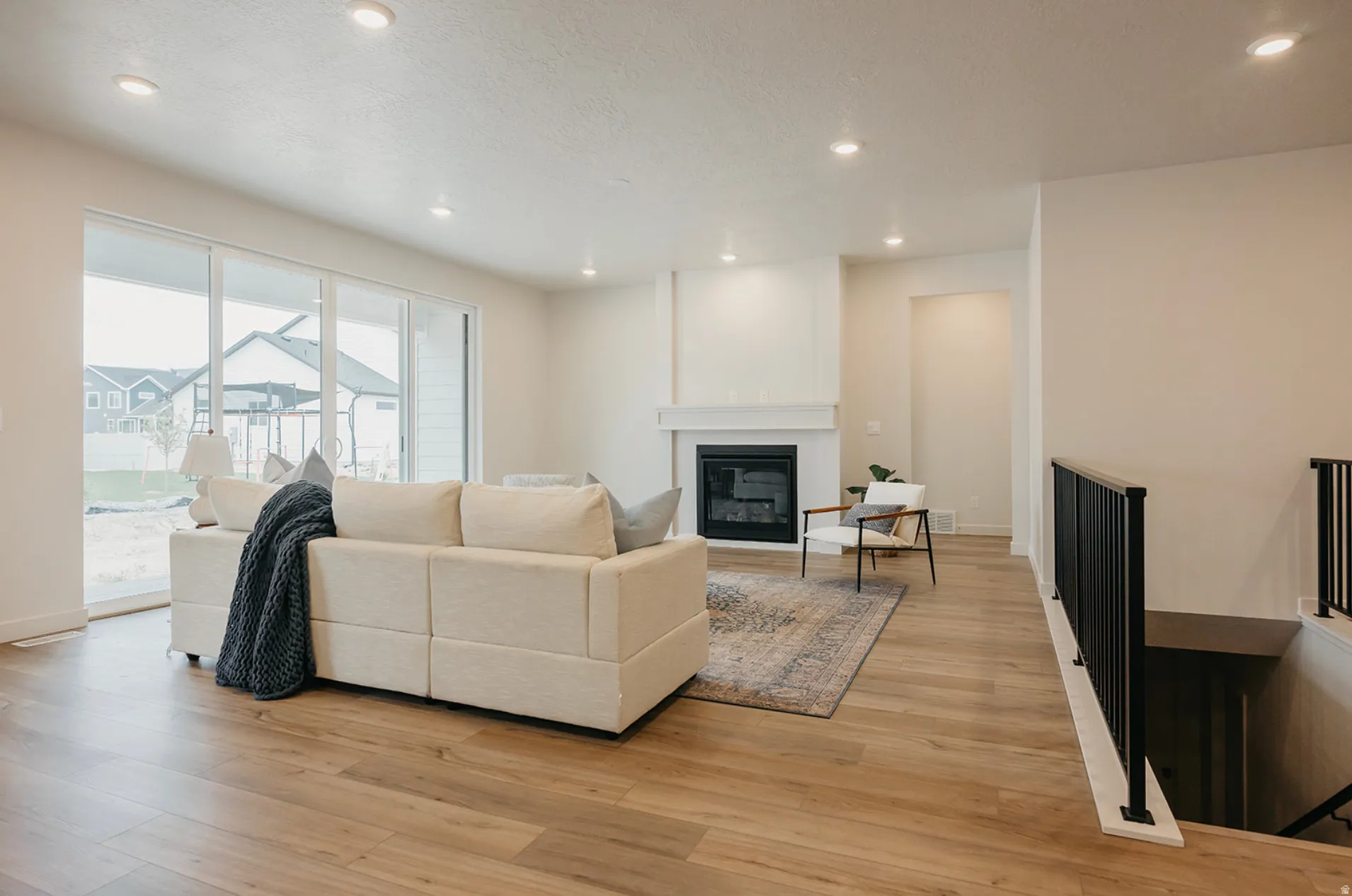 Spacious living area featuring wood-finish flooring, a fireplace with a white mantel, and recessed lighting