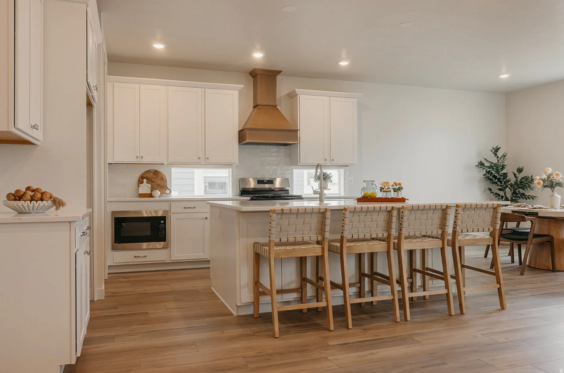 Open-concept kitchen featuring white cabinetry, a built-in microwave, a large central island with seating, a bronze range hood, and wood-finish flooring