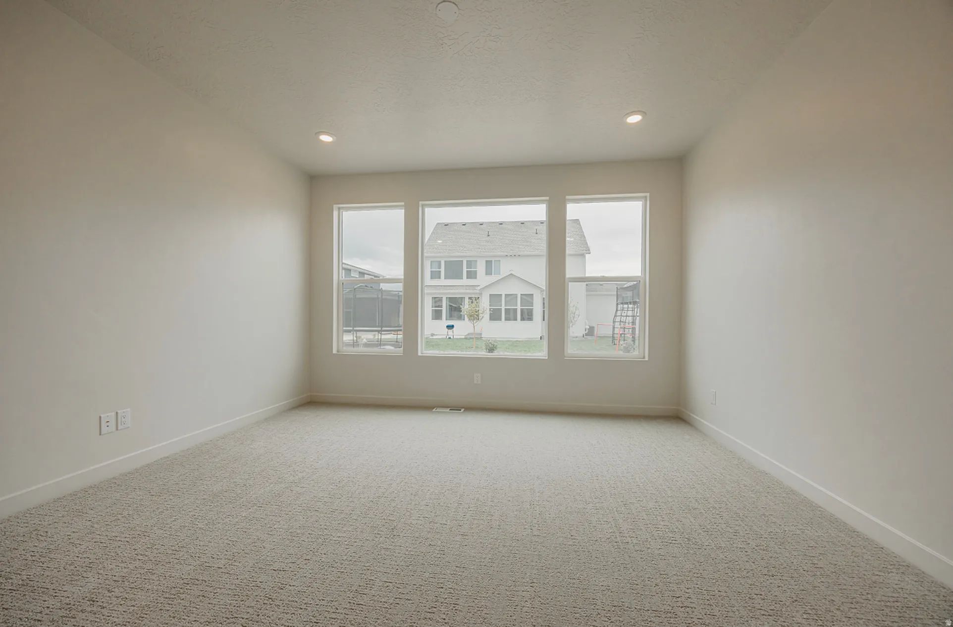 Bright room featuring three large windows, recessed ceiling lighting, light-colored carpet, and white baseboards