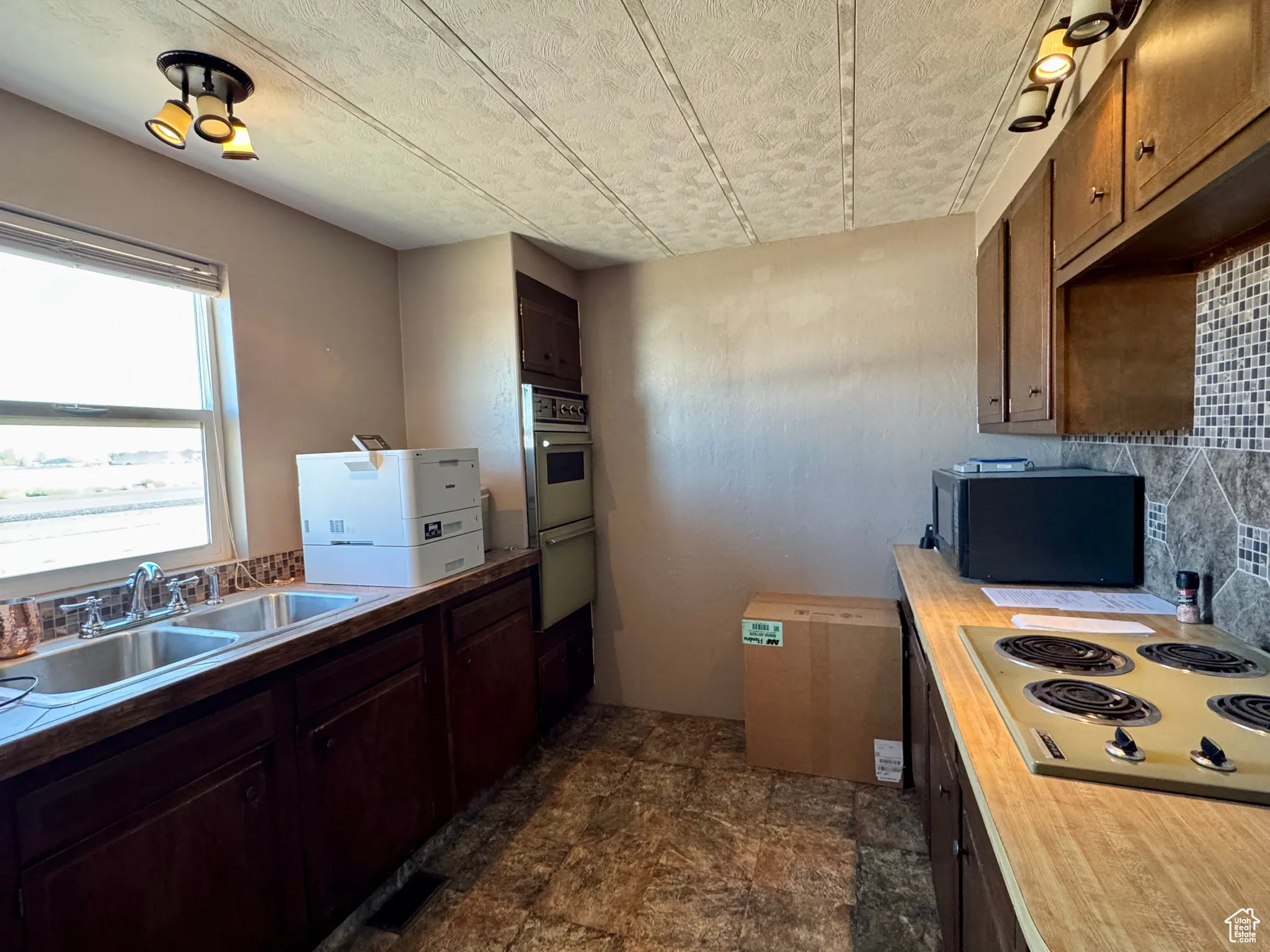 Kitchen with electric stovetop, black microwave, a textured ceiling, stone finish flooring, and light countertops