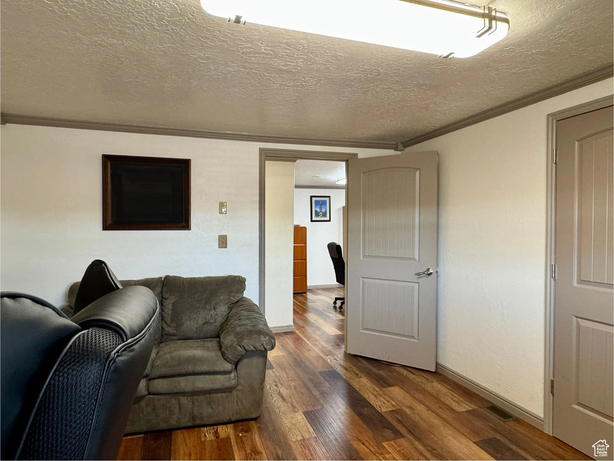 Living area with a textured ceiling, ornamental molding, dark wood finished floors, and a desk