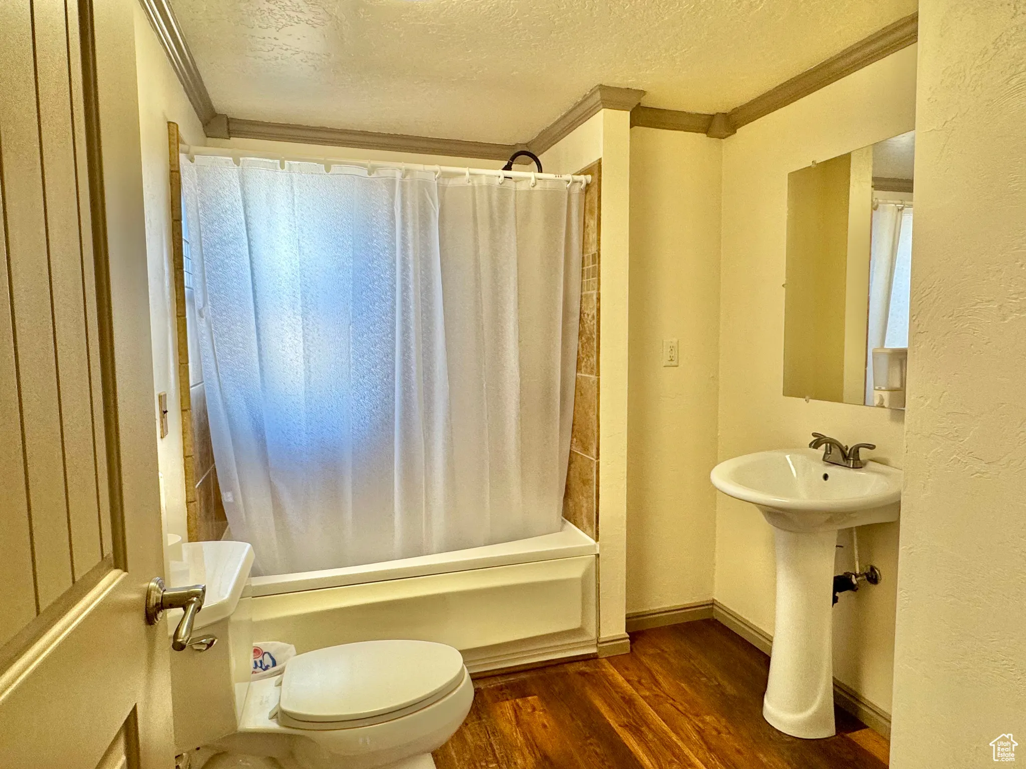 Bathroom featuring a textured ceiling, ornamental molding, dark wood finished floors, shower / tub combo, and a textured wall