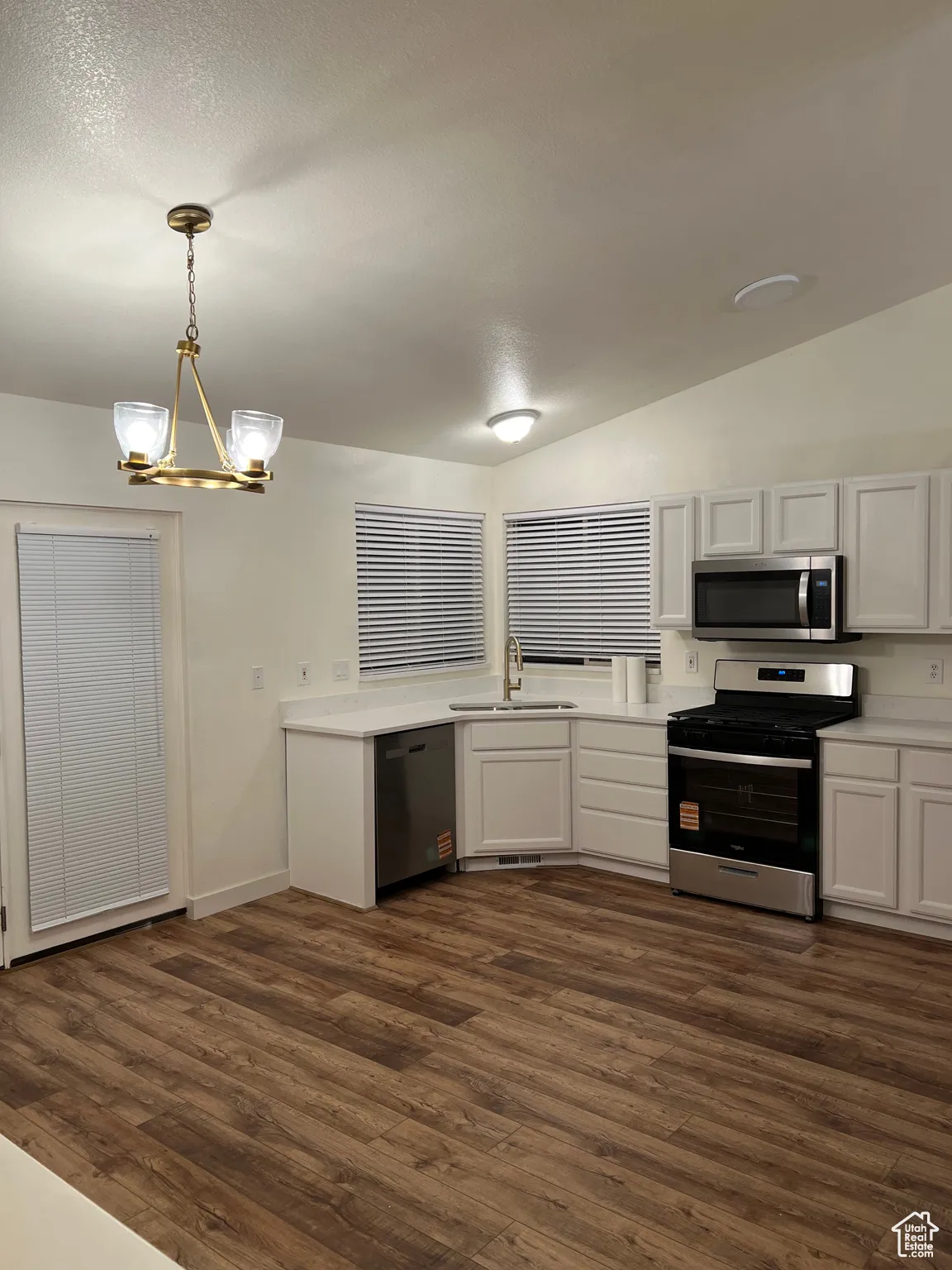 Kitchen featuring white cabinets, stainless steel appliances, dark wood finished floors, a chandelier, and lofted ceiling