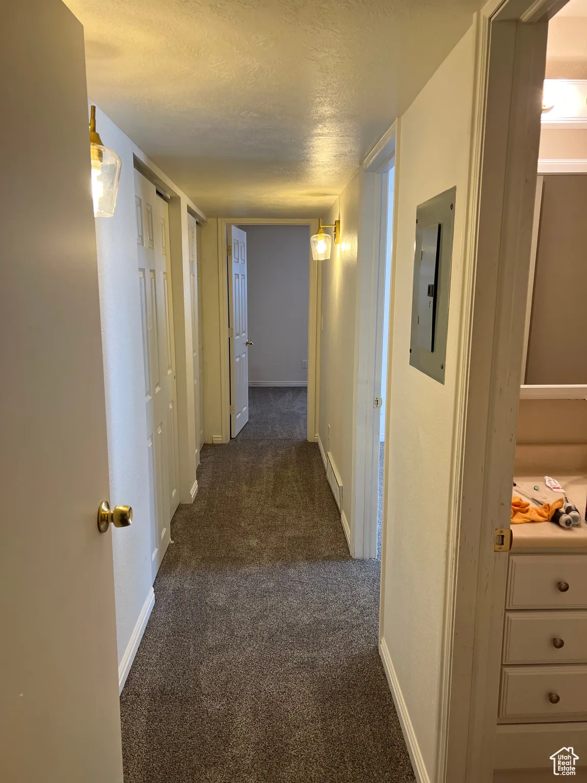 Hall featuring dark carpet, a textured ceiling, and electric panel