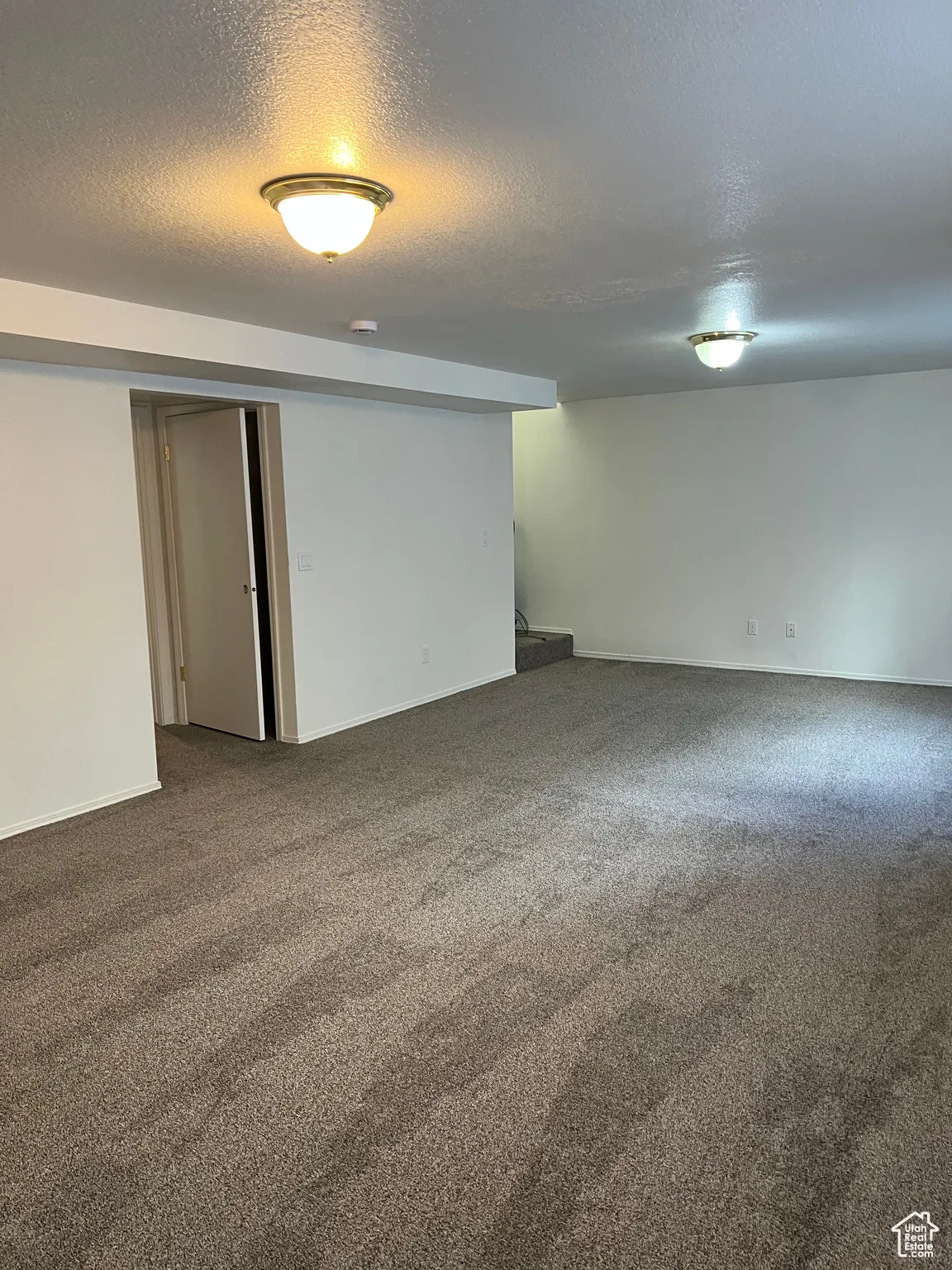 Large family room in basement featuring a textured ceiling and carpet floors