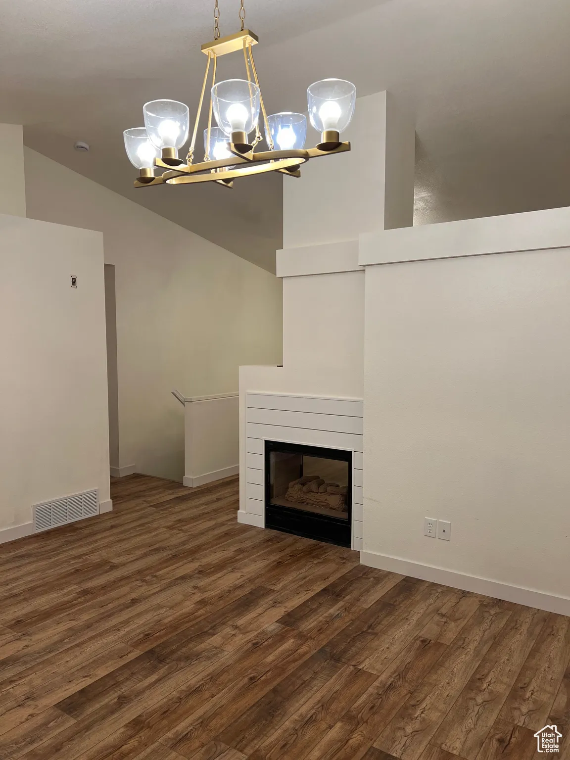 Unfurnished living room with dark wood-type flooring, lofted ceiling, a glass covered fireplace, and a chandelier