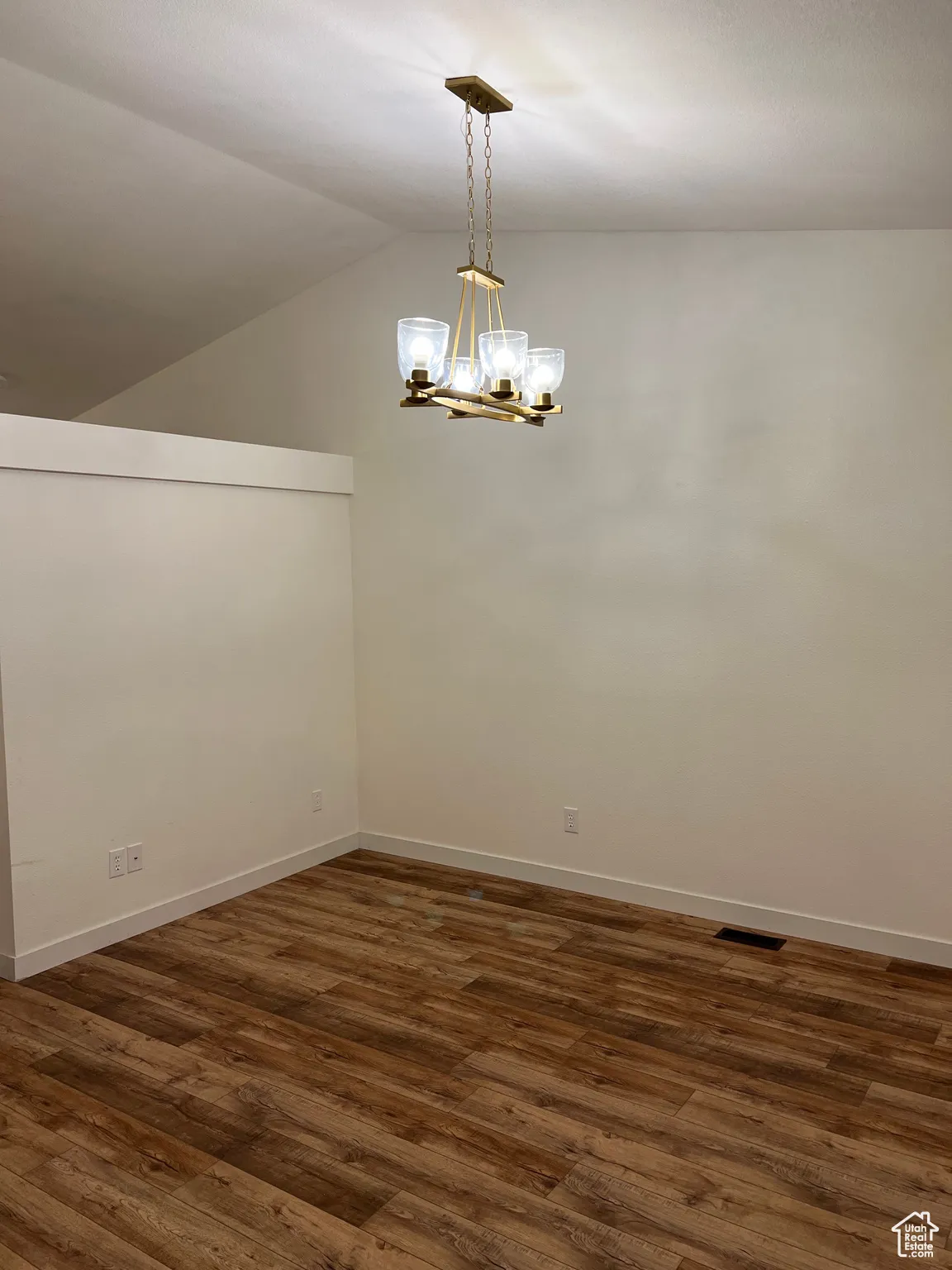 Unfurnished room featuring lofted ceiling, dark wood finished floors, and a brushed gold chandelier