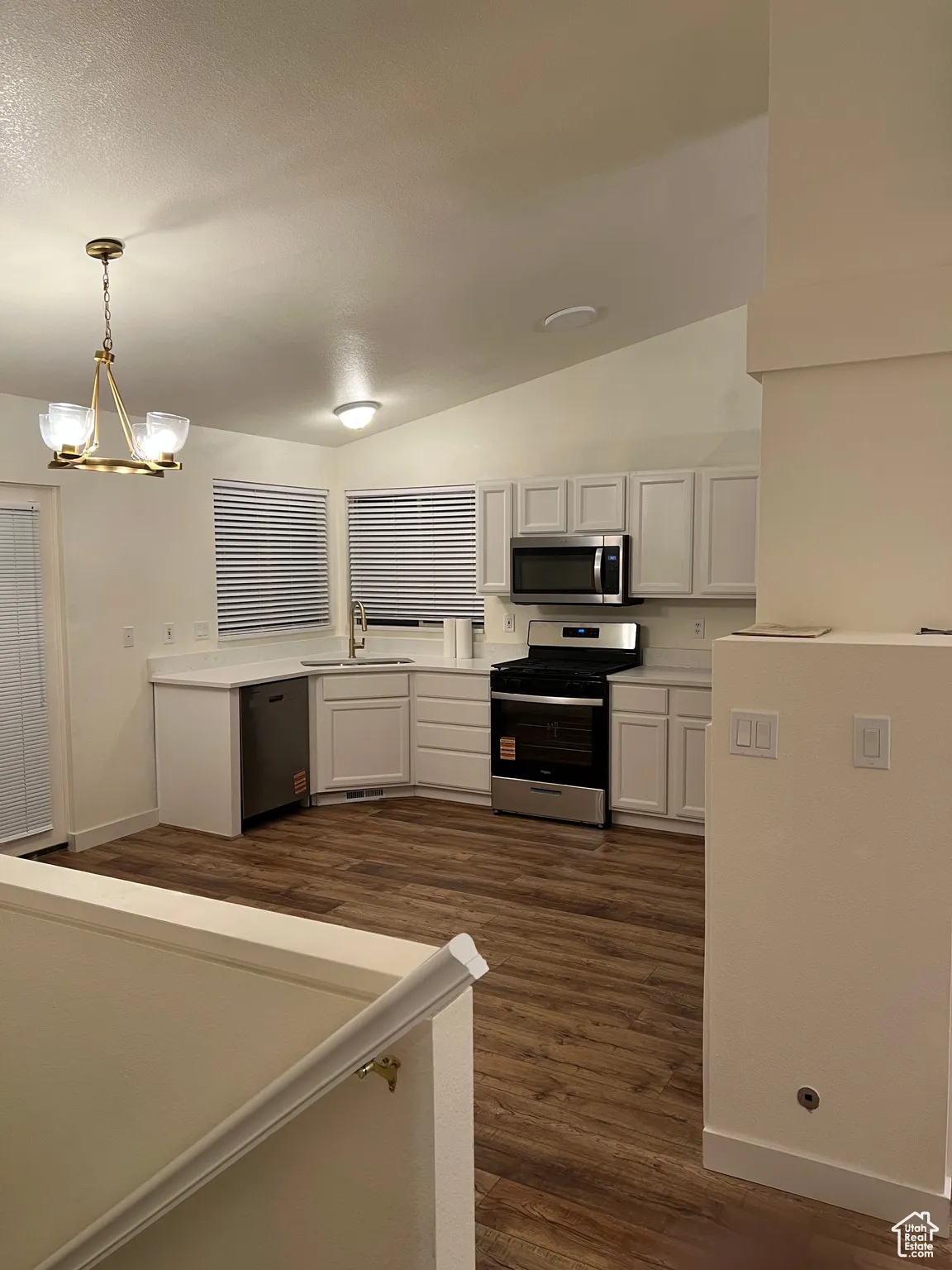 Kitchen featuring white cabinetry, dark wood-style floors, appliances with stainless steel finishes, lofted ceiling, and a chandelier