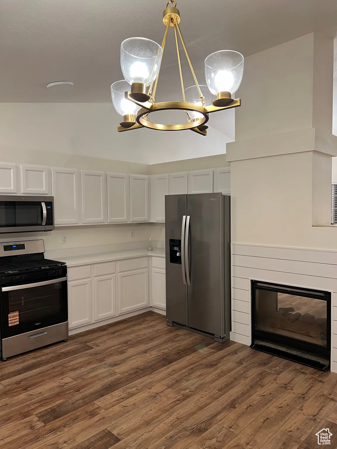 Kitchen with stainless steel appliances, white cabinetry, dark wood-type flooring, a chandelier, and hanging light fixtures