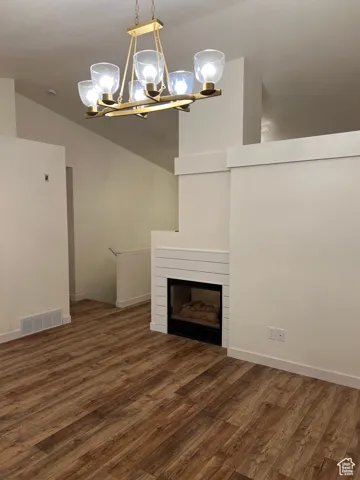 Unfurnished living room with dark wood-type flooring, lofted ceiling, a glass covered fireplace, and a chandelier
